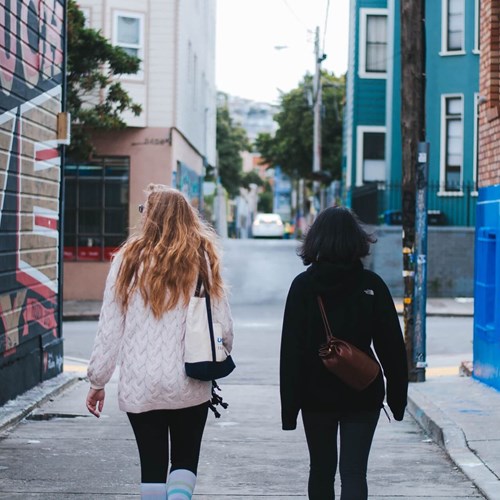 Two women walking down a graffitied street 