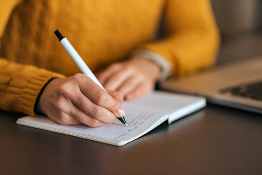 Person in a yellow jumper writing in notebook with a pen