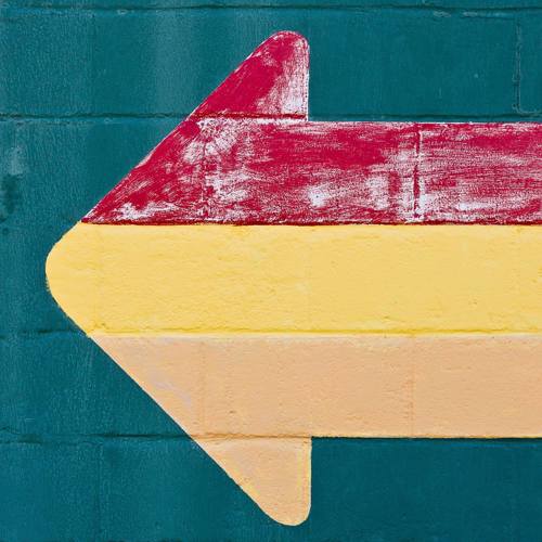 A large colourful arrow painted onto a brick wall pointing right to left