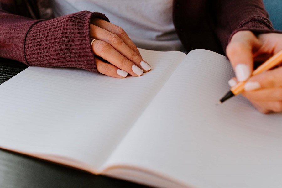 Close up shot of a young woman's hands looking as though she is about to write in a large hardback notebook