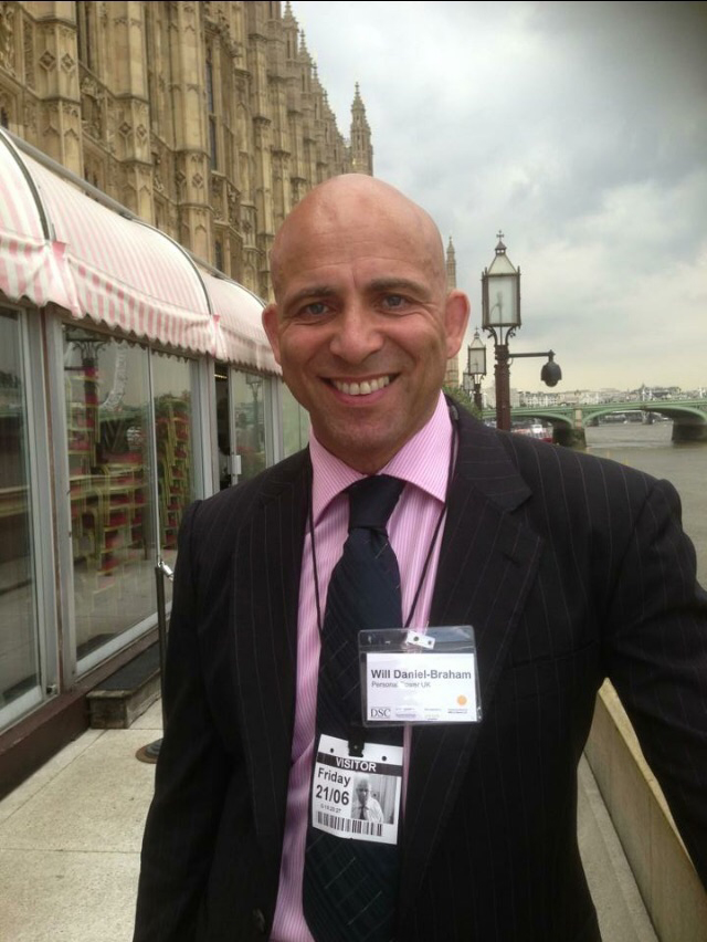 Image of Will Daniel-Braham in a suit standing in front of Parliament of the Thames River