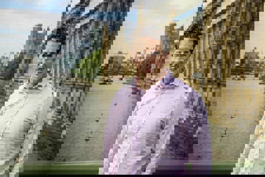 Head and torso image of Johnny Mercer MP standing on a bridge infront of Parliament 